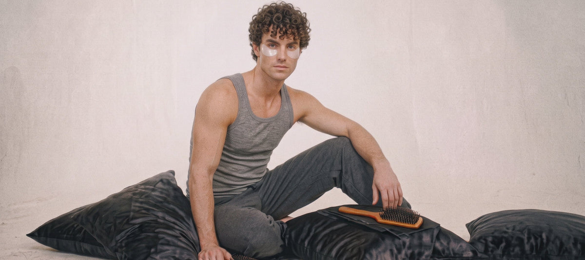 Homme aux cheveux bouclés assis sur des coussins en satin noir
